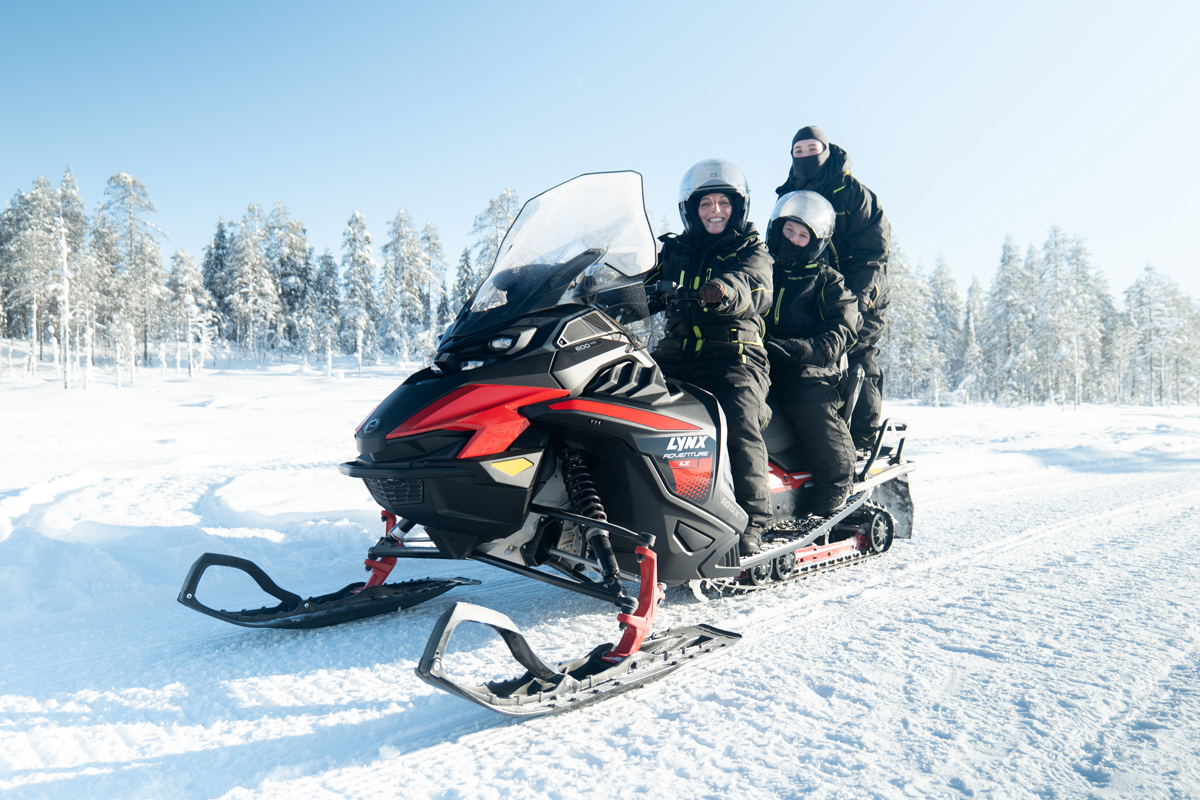 Family riding a snowmobile through snow-covered forests on a private safari in Lapland.
