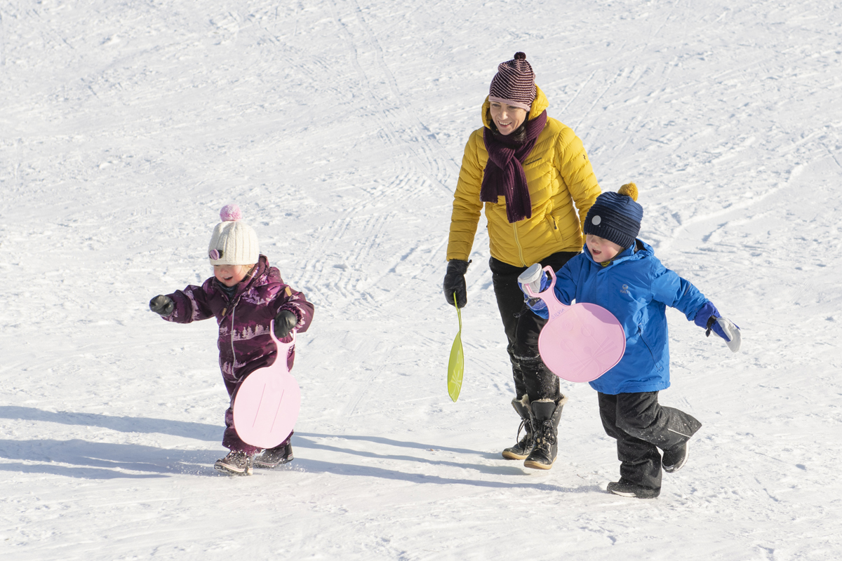 Two children tobogganing with a parent on a sunny winter day in Finnish Lapland.