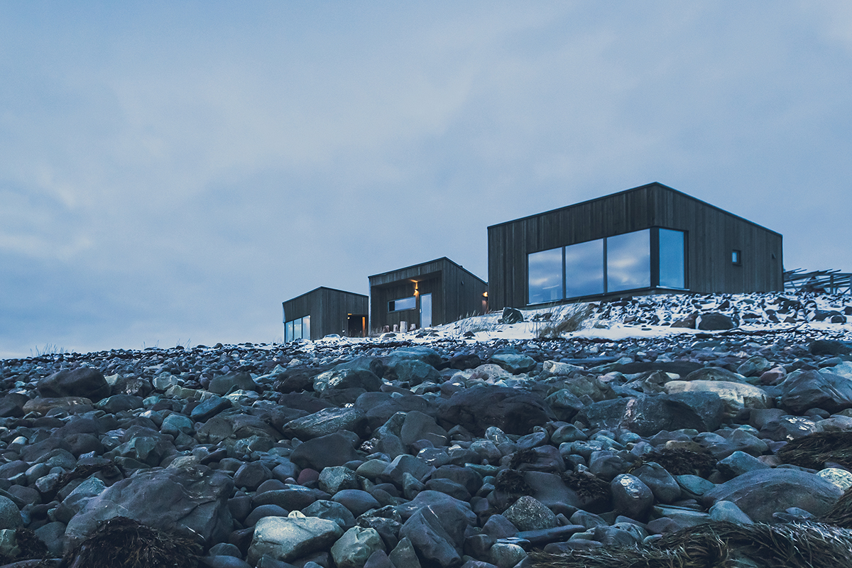 Des chalets en bois sombre sur le littoral rocheux du Varanger Lodge, en Norvège.
