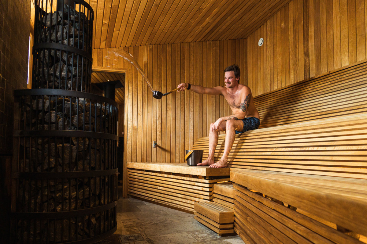 Un homme versant de l'eau sur les pierres chaudes d'un sauna traditionnel en bois.