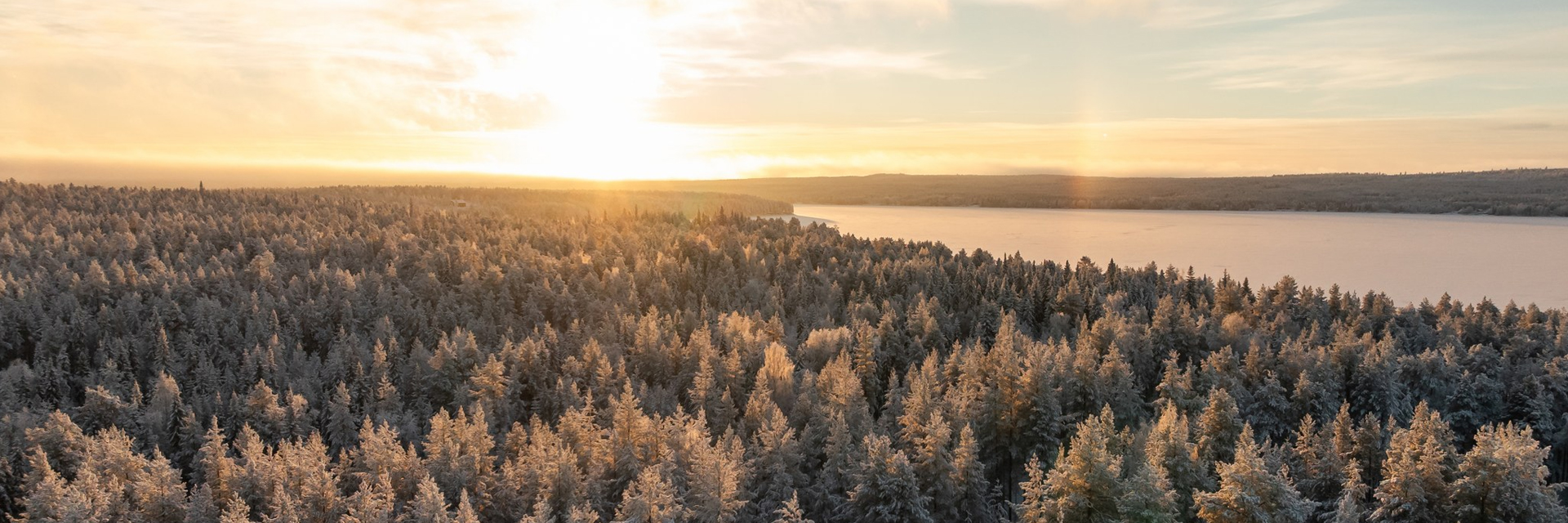 Aerial view of frost-covered pine forest and a wide river at sunrise between Rovaniemi and Levi.