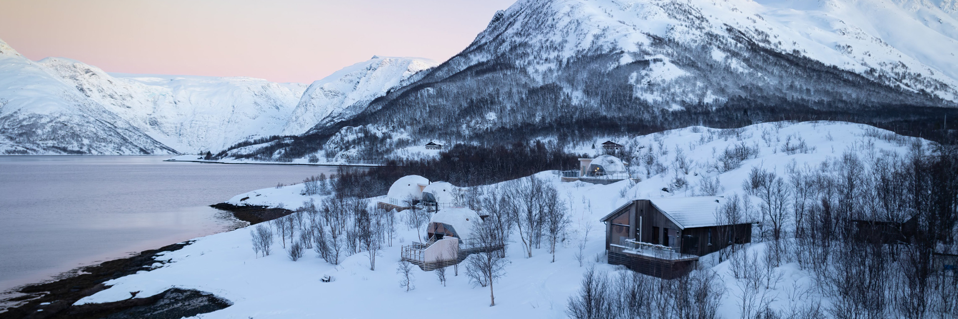 Wide view of Isbreen's igloos and cabins along the fjord, framed by snow-covered mountains.