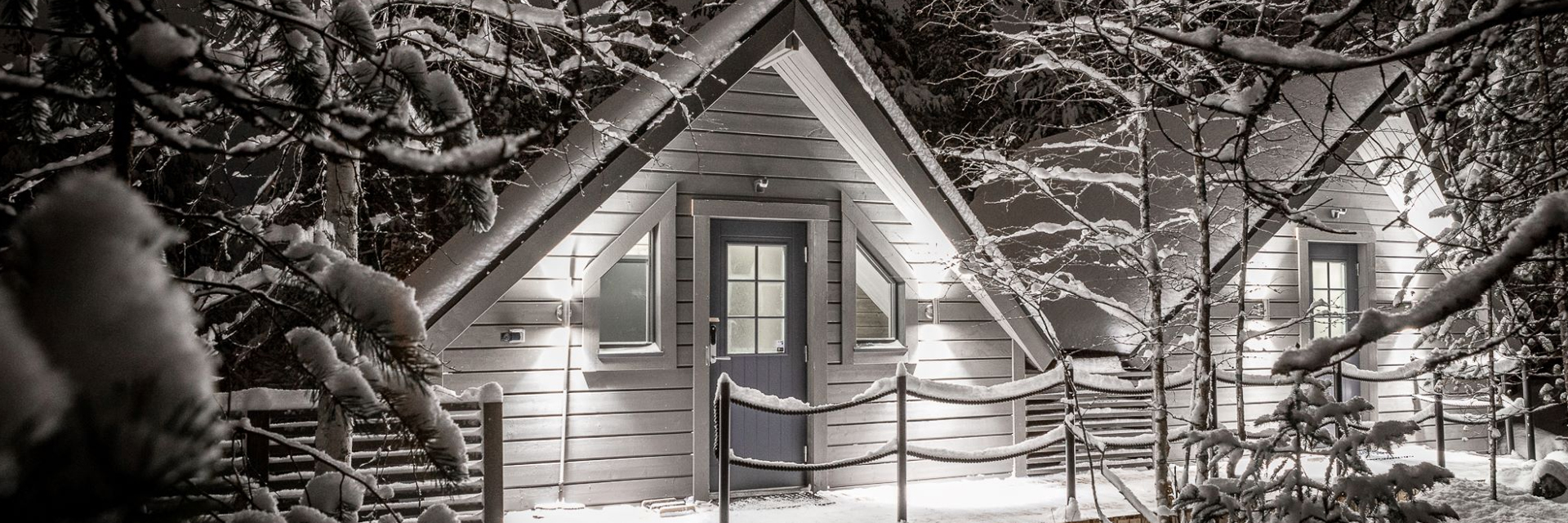 Lit A-frame cabin at night surrounded by snow-covered trees, Pyhä, Finnish Lapland
