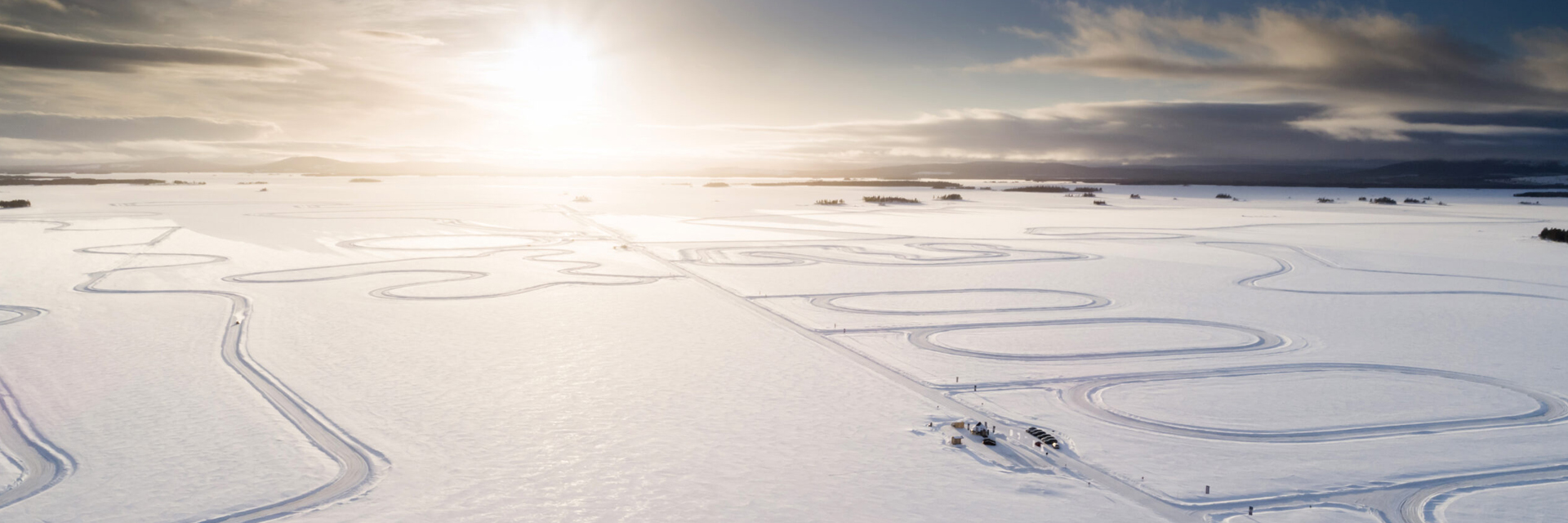 Aerial view of a frozen lake in Swedish Lapland with car tracks tracing circuits across the ice under a low winter sun.