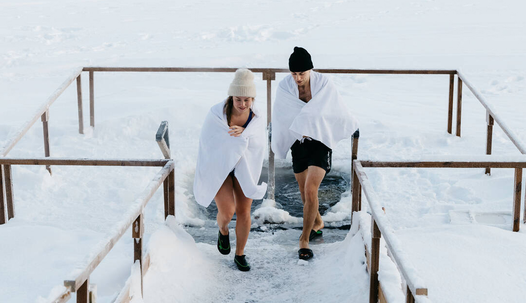 Adventure and Wellness in Lapland. Ice swimming in a frozen lake in the Arctic forest.